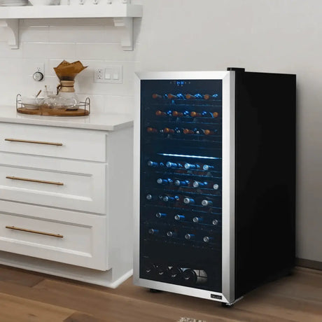 Freestanding wine fridge with stainless trim and LED-lit shelves, storing 50–99 wine bottles beside modern white kitchen cabinetry.